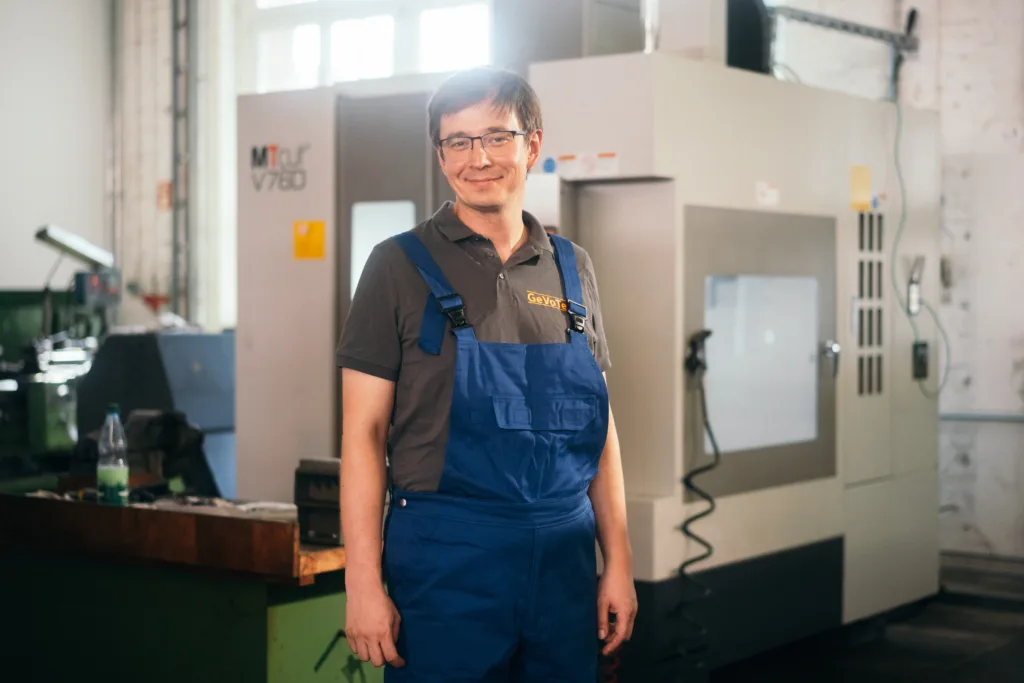 Technician in blue overalls standing in front of a CNC machine at a workshop